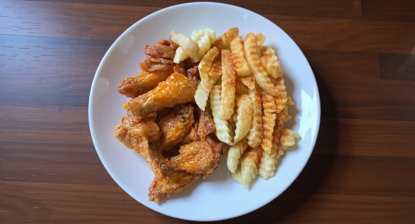 A wing restaurant's own phone photo of wings and fries in a takeout box, and the same food on a plate after enhancement with MenuPhotoLab