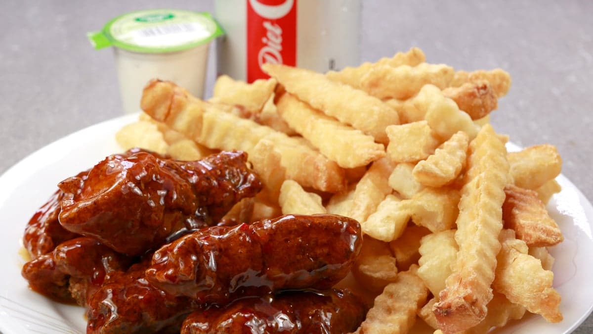 A close-up phone photo of glazed wings and crinkle fries on a white plate with a ranch cup and a soda can behind, from another location's DoorDash listing