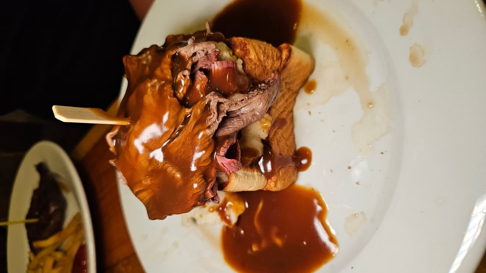 Phone photo of an open-faced roast beef sandwich covered in gravy, shot sideways in a dim restaurant